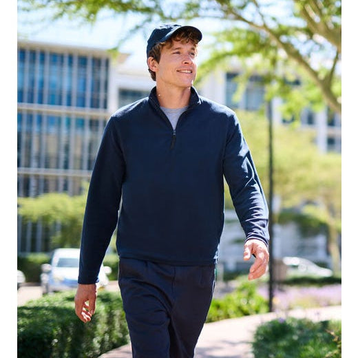A man walking outdoors on a sunny day, wearing a dark navy blue long-sleeve quarter-zip pullover and matching shorts.